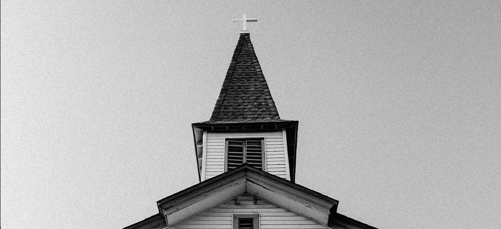 Torre de uma igreja com a cruz no alto, em preto e branco